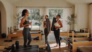 Boutique reformer Pilates studio owner chatting with smiling members holding yoga mats after class
