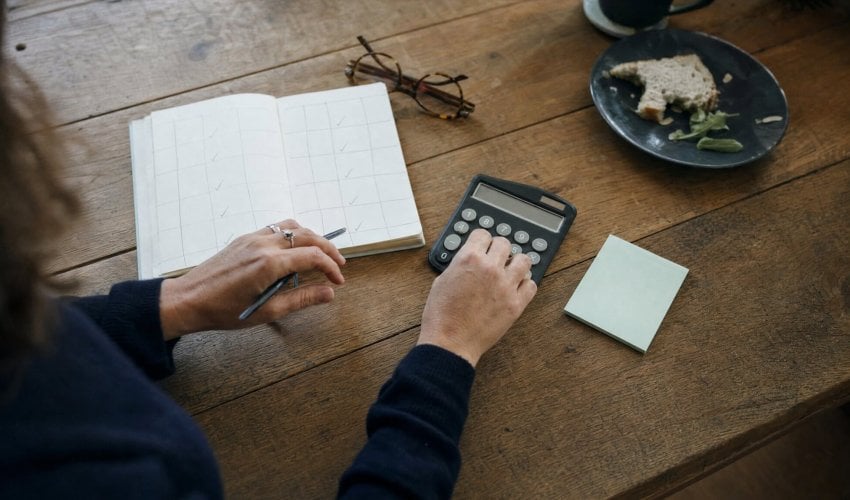 Hands using a calculator next to a planner on a wooden desk